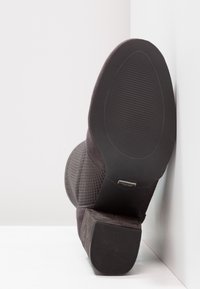 Szare zamszowe botki na wysokim obcasie z teksturowaną cholewką, płaską gumową podeszwą i wyraźnym obcasem. Udekorowane małym metalowym akcentem w pobliżu obcasa.