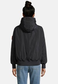 Veste bomber noire avec capuche, poignets élastiques et ourlet. Présente une texture de tissu lisse et une patch sur le bras supérieur.