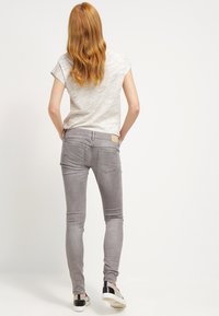 Vaqueros ajustados grises con cintura de altura media, diseño de cinco bolsillos y sutiles detalles de costura, combinados con una camiseta corta de color gris claro.