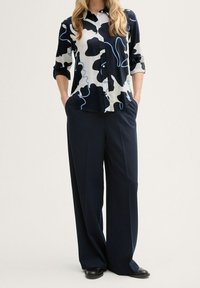 Chemise collerette de couleur marine, crème et motif abstrait noir, assortie à un pantalon taille haute marine. Tissu lisse, coupe décontractée et manches retroussées.