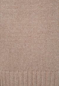 Beige stickad tyg med en mjuk textur, med ett slätt slätstickningsmönster och ribbad kantdetalj längst ner.