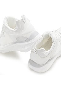 White athletic shoes featuring a mesh upper, padded collar, textured accents, and a rubber sole with a textured grip pattern.