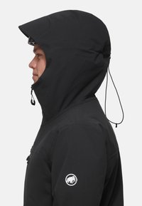 Black waterproof jacket with a hood and binding, featuring a zipper and a logo patch on the left sleeve. Smooth outer texture.