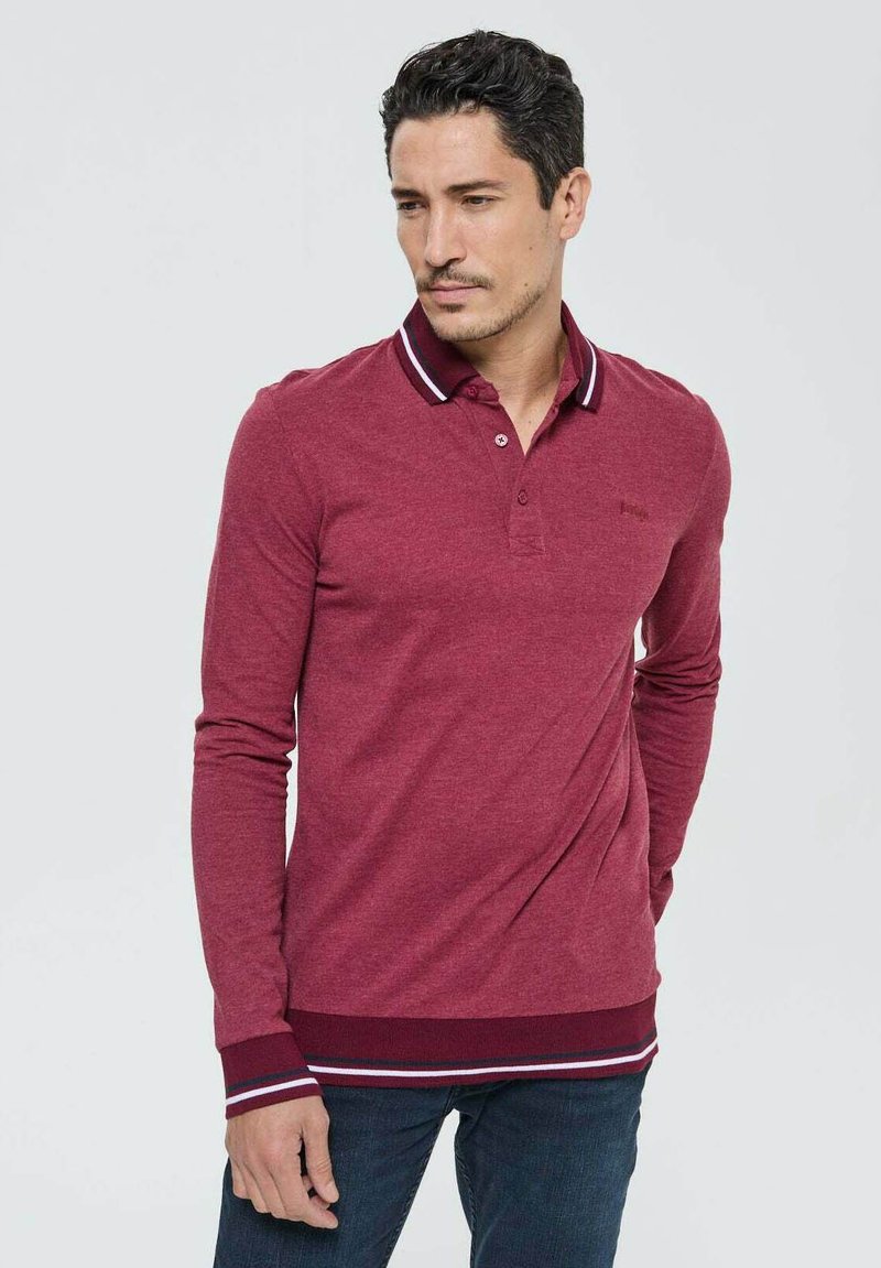 Polo long à manches longues bordeaux avec un col à rabat, accents rayés au niveau du col et de l'ourlet, présentant une texture douce et une coupe décontractée.