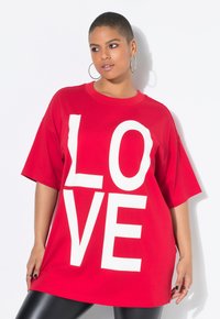 T-shirt oversized in cotone rosso con grande scritta bianca "LOVE". Maniche corte e scollatura rotonda, abbinato a leggings neri lucidi.