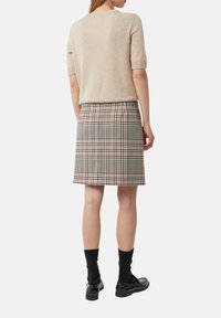 Beige kortemouwen trui gecombineerd met een geruite rok in zwart, beige en bruin tinten; model draagt zwarte sokken en schoenen.