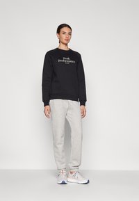 Schwarzer Sweatshirt mit dem Text "Peak Performance", graue Jogginghosen und weiße Sportschuhe mit orangefarbenen und blauen Akzenten. Glatter Stoff, lockere Passform.