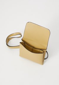 Petit sac bandoulière structuré en cuir beige avec rabat ouvert, montrant deux compartiments intérieurs et une fine sangle d'épaule.