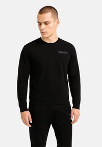 Felpa nera con scollo rotondo realizzata in tessuto morbido, con un discreto logo "Cristiano Ronaldo Nightwear" sul petto e polsini a costine.