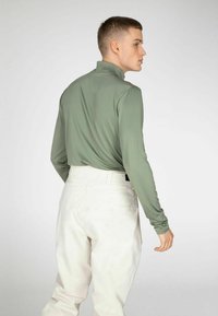 Lange mouwen, lichtgroen shirt met hoge kraag, gecombineerd met witte broek. Gladde textuur, getailleerd ontwerp en minimalistische styling.