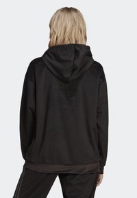 Svart hoodjacka i manchester med ribbad struktur, som har en avslappnad passform och en fåll som sträcker sig något nedanför midjan.