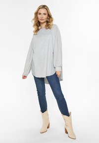 Lys grå langærmet top med rund halsudskæring, lagdelt design og sidelæg, parret med blå skinny jeans og beige cowboystøvler.