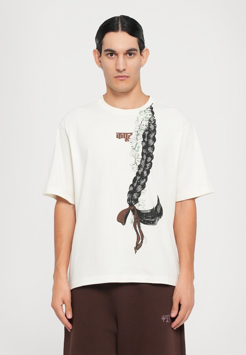 Cremfarbener T-Shirt mit kurzen Ärmeln, das eine Illustration von schwarzem geflochtenem Haar mit weißen Blumen und braunen Akzenten zeigt. Lässige, lockere Passform.