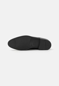 Semelle de chaussure noire en cuir avec un matériau en caoutchouc lisse, de forme arrondie et un motif de grip texturé. Présente un détail de logo embossé.