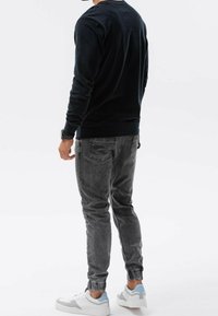 Camicia a maniche lunghe blu scuro, jeans grigi a sigaretta e scarpe da ginnastica bianche con accenti blu chiaro, viste da dietro su uno sfondo bianco.