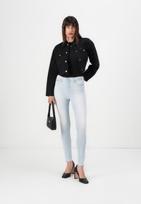 Čierna denimová bunda s gombíkmi, čierne body, svetlo modré skinny džínsy a čierne vysoké podpätky. Malá čierna kabelka s akcentom.