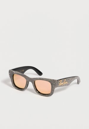 Lunettes de soleil rectangulaires noires avec des verres teintés rose et une monture couverte de petits points blancs, avec un logo Ray-Ban doré sur la branche.