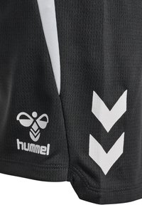 Sort sportstof med hvid hummel-bi-logo og to hvide chevronstriber nedad på sidepanelet af shorts eller trøje.