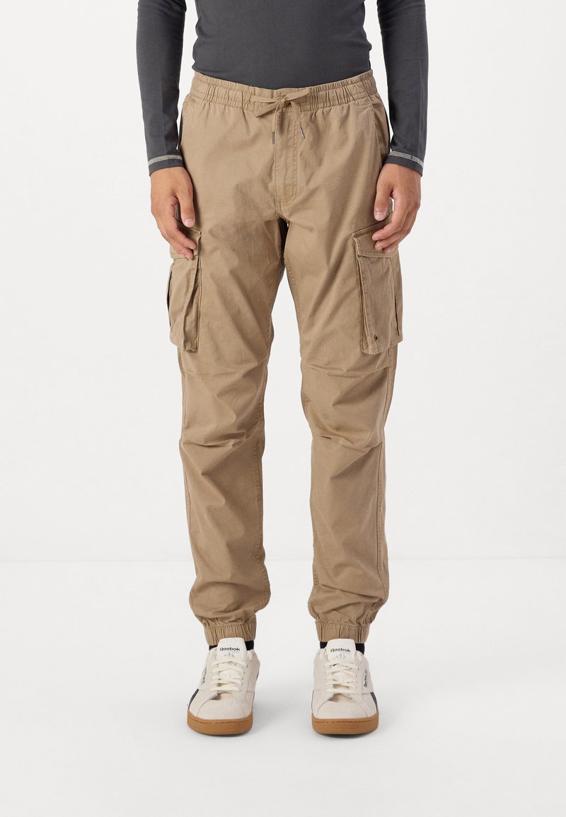 Beige cargo pants with an elastic waistband and cuffs, featuring two side pockets and a casual fit. Made from durable, lightweight fabric.