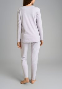 Maglia grigia chiaro a maniche lunghe con scollatura rotonda abbinata a leggings bianchi con un sottile motivo a pois. Materiale in cotone morbido.