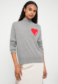 Szürke kötött pulóver magas nyakkal, piros szív grafikával és "FUTURE" felirattal. Texturált anyag, laza szabás, bordás mandzsetták és szegély.