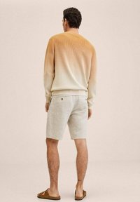 Kevyt neulepaita, jossa on liukuvärjäys beigeistä hailakkaan valkoiseen, yhdistettynä vaaleanharmaisiin shortseihin. Rentoa pukeutumista täydentävät kevyet kengät.