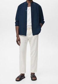 Laivastonsininen napillinen paita, valkoinen toppi, vaaleanbeige pellavahousut ja mustat sandaalit. Paidassa on mandariinikaulus ja rento istuvuus.