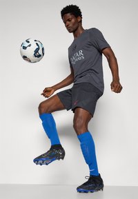 Czarne szorty sportowe z teksturowanym wzorem, szara koszulka z logo "Qatar Airways", niebieskie skarpety piłkarskie oraz czarne korki z niebieskimi akcentami.