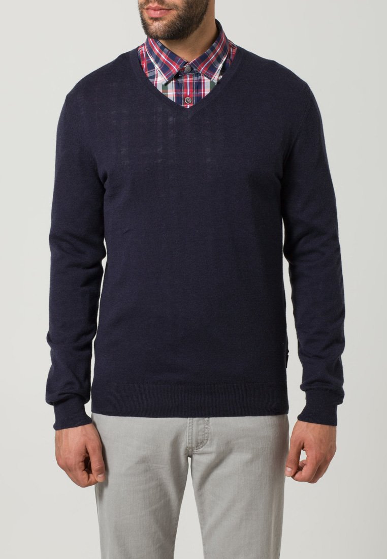 Marineblaue Strickjacke mit V-Ausschnitt, getragen über einem rot-blau karierten Hemd. Hat lange Ärmel sowie gerippte Bündchen und Saum.
