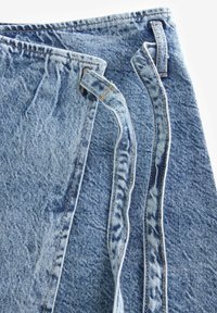 Denim tkanina u svijetloplavoj boji s teksturiranom površinom. Ima šivene šavove, petlje za remen i neuredan rub s desne strane.