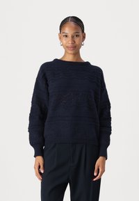 Maglione lavorato a maglia blu navy con motivi testurizzati, vestibilità ampia e orlo a coste. Presenta maniche larghe e scollatura rotonda. Materiale morbido.