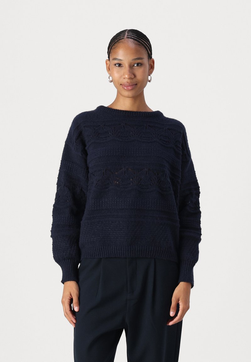 Maglione lavorato a maglia blu navy con motivi testurizzati, vestibilità ampia e orlo a coste. Presenta maniche larghe e scollatura rotonda. Materiale morbido.