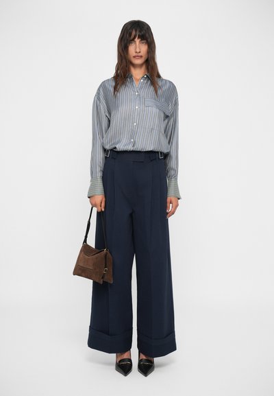 Cămașă dungată cu mâneci lungi, pantaloni evazați navy, și o geantă din suede maro. Încălțămintea constă în tocuri negre ascuțite.