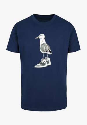 Marineblauwe katoenen t-shirt met een afbeelding van een meeuw die witte en grijze sneakers draagt, staande op twee benen, met een eenvoudig ontwerp.