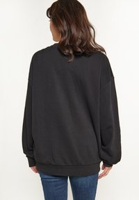 Sudadera negra de gran tamaño hecha de mezcla de algodón, con hombros caídos, mangas largas y dobladillo acanalado, combinada con jeans azules.
