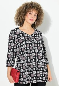 Tunique noire à motif floral en blanc et rouge, avec un col en V et des manches trois-quarts. Tient une pochette matelassée rouge.