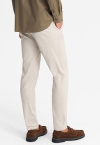 Chinos beige hechos de un tejido ligero, con pierna ajustada y bolsillos laterales, combinados con zapatos de ante marrón y una camisa verde olivo oscura.