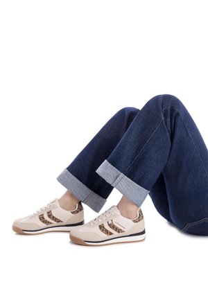 Zapatillas beige con detalles de estampado de leopardo, textura suave y cordones blancos. Combinadas con unos jeans de mezclilla azul oscuro arremangados que muestran un forro gris claro.