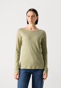 Langermet, lys grønn topp i et mykt, teksturert stoff med båtutringning. Kombinert med blå jeans gir antrekket en uformell og avslappet stil.