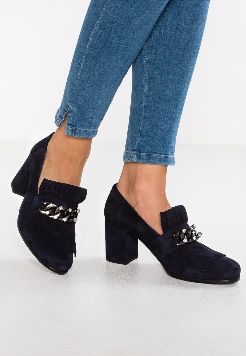 Chaussures à talons en daim bleu marine avec un ornement de franges et de perles sur l'empeigne, un talon épais et des côtés ouverts.