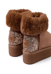 Botas tobilleras marrones con un cálido collar de piel sintética, detalles brillantes en los laterales y un acabado suave de ante. Suelas planas y detalles de hardware con marca.