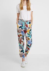Pantaloni jogger con stampa floreale multicolore, dotati di vita elastica e cordino, abbinati a una semplice t-shirt bianca a maniche corte e sneakers.