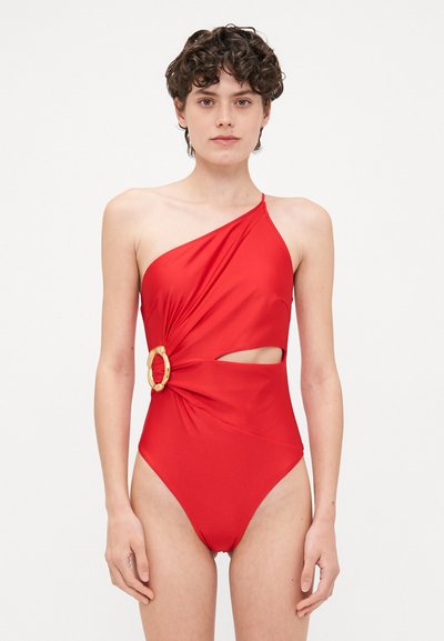 Rode eenpiece badpak met een asymmetrisch ontwerp, met een gedraaide voorkant en een ronde gouden accent op de taille. Glad stofoppervlak.