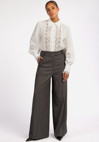 Witte blouse met kantdetails en knoopfront. Grijze gestreepte broek met wijde pijpen. Gladde stof, gestructureerde pasvorm en puntige schoenen.