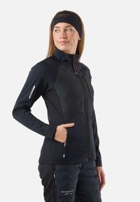 Giacca nera con cerniera e design geometrico testurizzato sul davanti, maniche lunghe, due tasche laterali e vestibilità slim. Abbinata a pantaloni neri imbottiti.