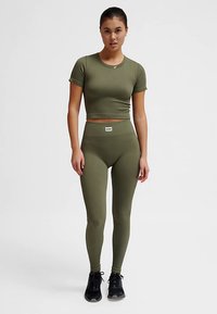 Olivengrøn ribbet crop top med korte ærmer kombineret med matchende højttaljede leggings, begge med et lille mærke med brandnavn på taljebåndet.