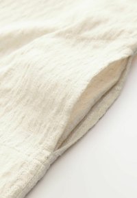 Helles beiges Textil mit einer subtilen Struktur, gefaltet mit einer glatten Kante, die Weichheit und ein natürliches Aussehen zeigt.