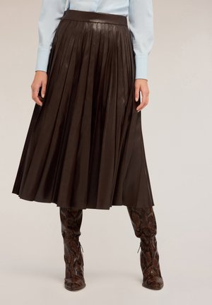 Kobieta ubrana w ciemnobrązową plisowaną spódnicę midi, dobraną do brązowych kozaków za kolano z wzorem skóry węża oraz jasnoniebieskiej koszuli.