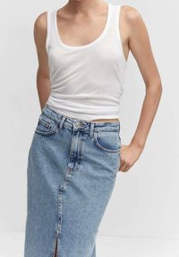 Valkoinen hihaton toppi yhdistettynä korkeavyötäröiseen siniseen farkkuhameeseen, jossa on etureikä ja klassinen viiden taskun muotoilu.