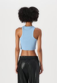 Lichtblauw topje met een korte lengte en een geribbelde textuur, met een ronde hals en brede armsgaten, gecombineerd met zwarte, glanzende, elastische broek met hoge taille.